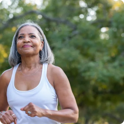 A woman with a smiling face amidst natural green surroundings.